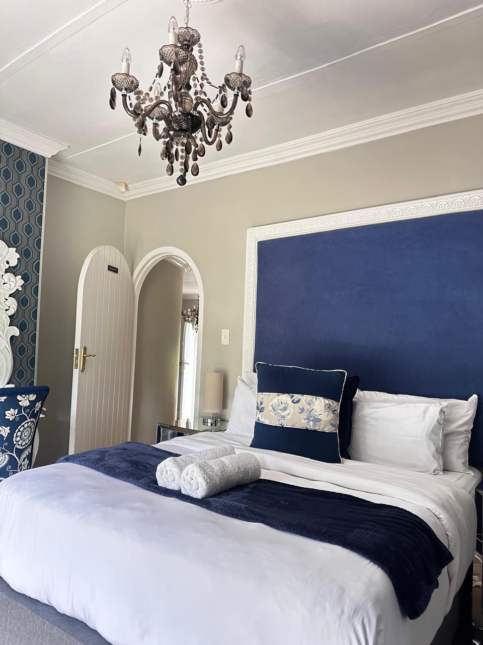 Room 2 queen bed with blue velvet headboard and chandelier